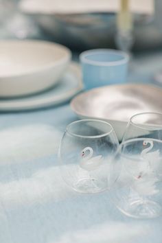 two wine glasses sitting on top of a blue table cloth next to plates and silverware