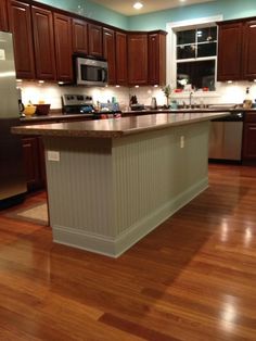 a large kitchen with wooden floors and stainless steel appliances in the center, along with dark wood cabinets