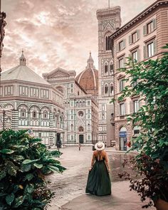 a woman in a green dress and hat is walking down the street with buildings behind her