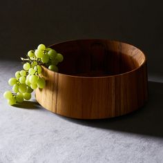 a wooden bowl filled with green grapes on top of a table