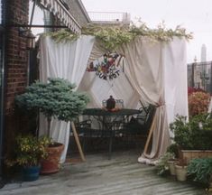 an outdoor patio covered in curtains and potted plants on top of a wooden deck