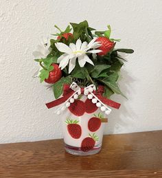 a vase filled with flowers and strawberries on top of a wooden table next to a wall