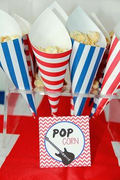 red, white and blue striped popcorn cups with pop corn in them on a table