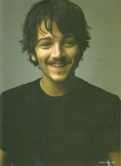 a man with a mustache and black shirt smiling at the camera while holding a cell phone in his hand