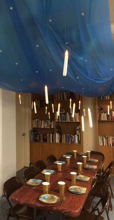 a long table with plates and cups on it under a blue tarp over bookshelves