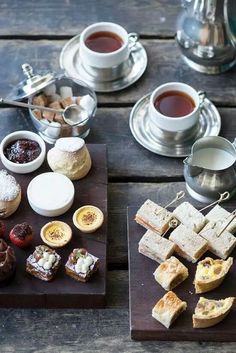 a table topped with two trays filled with different types of food and cups of tea