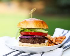 a hamburger with lettuce, tomato and onion on a plate next to fries