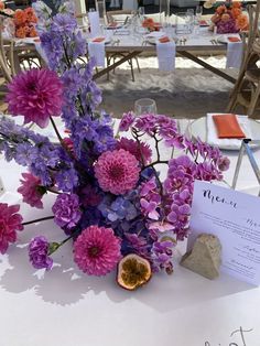 purple flowers are in a vase on a table at an outdoor wedding reception with menus and place cards