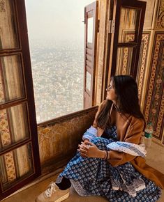 a woman sitting on top of a window sill looking out at the city below