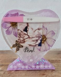 a purple heart shaped vase with flowers and butterflies on the front, sitting on a wooden table