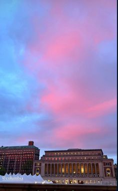 the sky is pink and blue as it sits above some buildings with lights on them