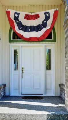 an american flag hanging over the front door of a building with two white doors and brick pillars