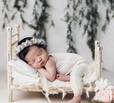 a baby is sleeping on a bed with white fur and flowers in her hair, wearing a flower headband