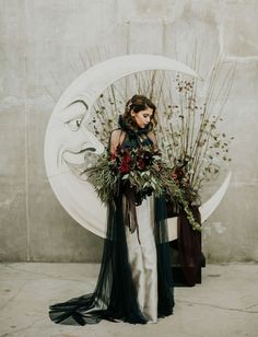 a woman standing in front of a white circle holding flowers and greenery on her head