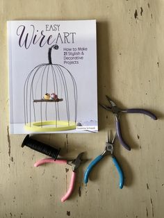 three pairs of scissors sitting on top of a table next to a book about easy wire art