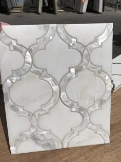 a white marble tile with an intricate design on it's side, sitting on top of a wooden table