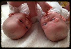 two baby babies laying on top of a white blanket with their hands touching each other's heads