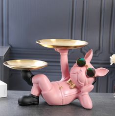 a pink pig figurine with two gold plates on it's back and one sitting on the ground