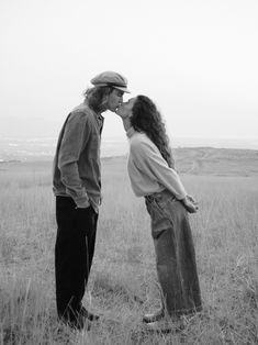 black and white photograph of two people kissing each other in an open field with mountains in the background