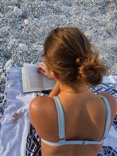 a woman sitting on the beach reading a book