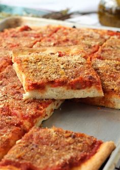 sliced pizza sitting on top of a pan with sauce and seasoning next to it