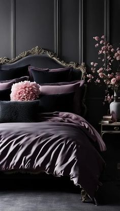 a bed with purple sheets and pillows in a dark colored room next to a vase filled with pink flowers