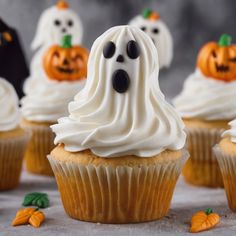 cupcakes decorated with white frosting and ghost faces are on a gray surface