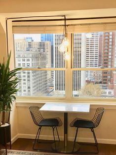 two chairs and a table in front of a large window with city buildings behind them