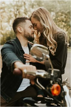 a young man and woman sitting on a motorcycle together, cuddling their foreheads