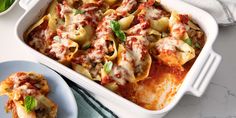 a casserole dish with meat and cheese on the side next to a plate of pasta