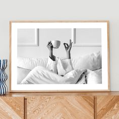 a black and white photo of a woman laying in bed with her feet up holding a coffee cup