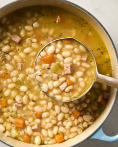 a pot filled with beans and ham on top of a stove next to a wooden spoon