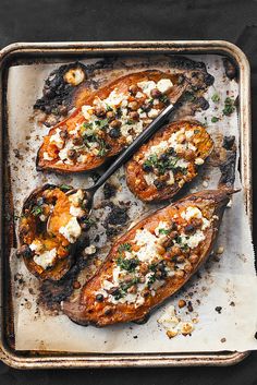 baked sweet potatoes topped with feta cheese and herbs on a baking sheet, ready to be eaten