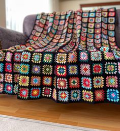 a crocheted granny blanket sitting on top of a wooden floor next to a couch