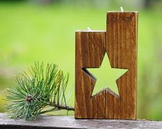 a wooden candle holder with a star cut out of it sitting next to a pine tree