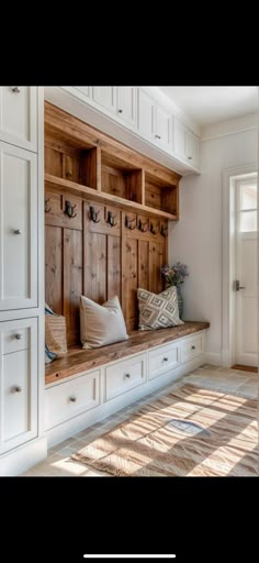 a wooden bench sitting in the middle of a room next to white cabinets and drawers