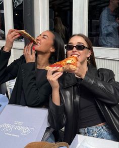 two women sitting at a table eating pizza