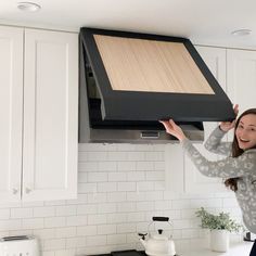 a woman is holding up a black stove hood