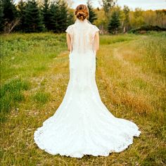 the back of a bride's wedding dress is shown in an open grassy field