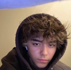 a young man with curly hair wearing a hoodie and looking at the camera while holding a cell phone to his ear