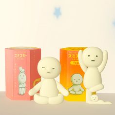 two small white dolls sitting next to each other in front of boxes with writing on them