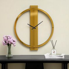 a gold clock on the wall next to a vase with flowers and reeds in it