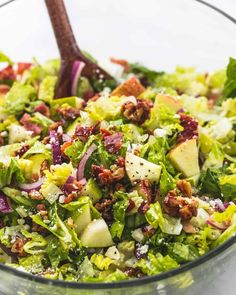 a salad with lettuce, red onions and cheese in a glass bowl next to a wooden spoon