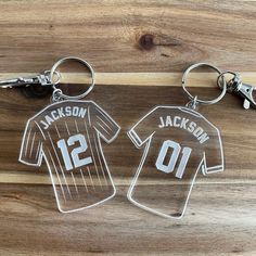 two personalized keychains with the name and number on them are sitting on a wooden surface