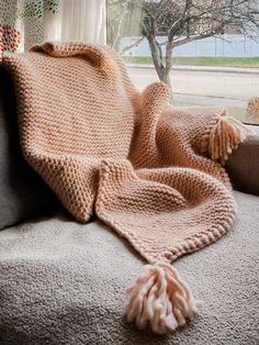 a blanket is laying on the back of a couch near a window with a tree in the background