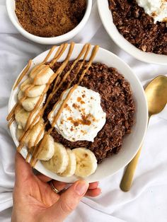 a person holding a plate with bananas, chocolate and whipped cream on it next to bowls of food