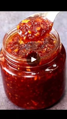 a spoon full of sauce sitting on top of a glass jar filled with something in it