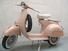 an old pink scooter is parked in front of a white wall and cement floor