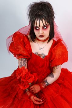 a woman in a red dress with makeup on her face and hands holding a flower