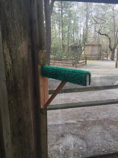 a green brush sticking out of the side of a wooden fence in front of a gate